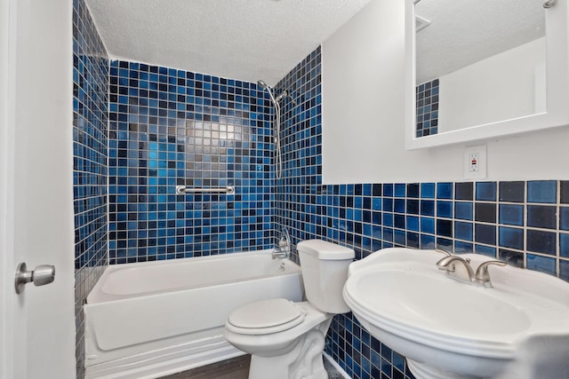 full bathroom with tile walls, toilet, a textured ceiling, washtub / shower combination, and a sink