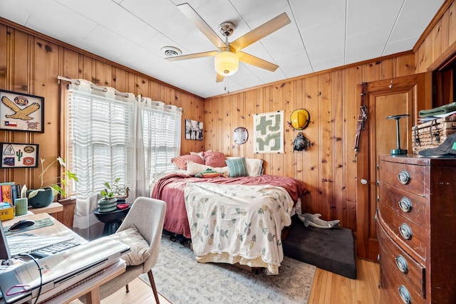 bedroom featuring wood walls, ceiling fan, and light hardwood / wood-style flooring