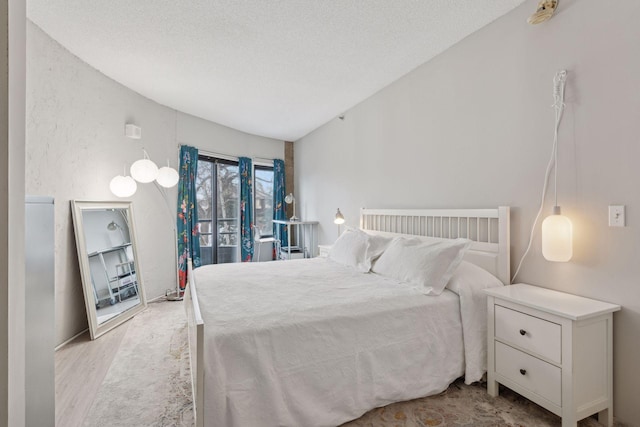 bedroom featuring lofted ceiling, a textured ceiling, and light hardwood / wood-style floors