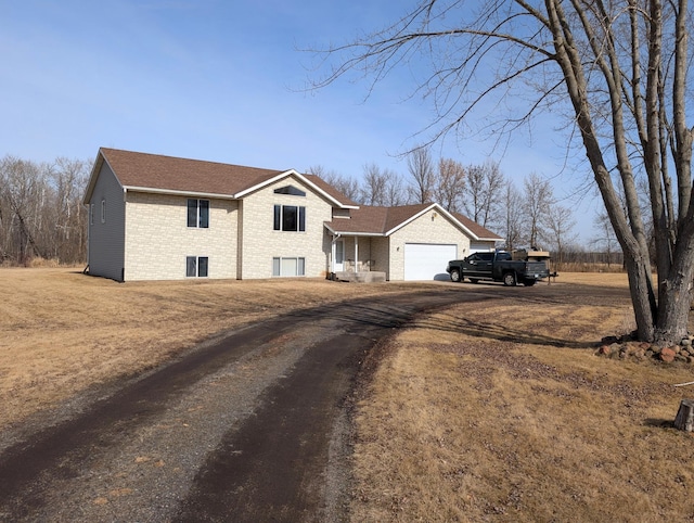 view of front facade featuring brick siding, a shingled roof, a garage, and dirt driveway