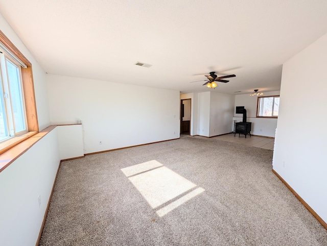 carpeted spare room with visible vents, baseboards, and a wood stove