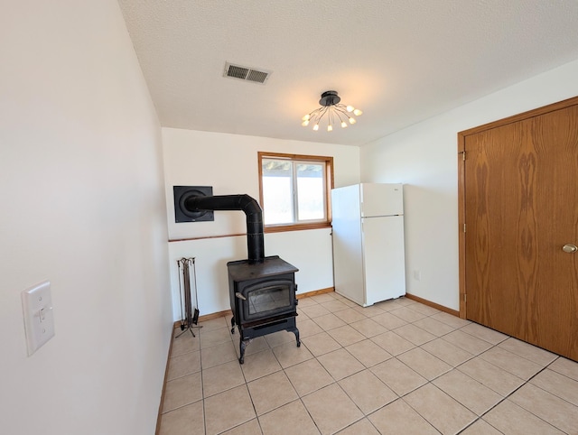 interior space with light tile patterned floors, baseboards, visible vents, a wood stove, and a textured ceiling