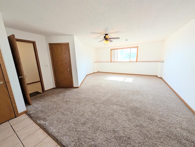 spare room featuring light tile patterned floors, a ceiling fan, baseboards, a textured ceiling, and light colored carpet