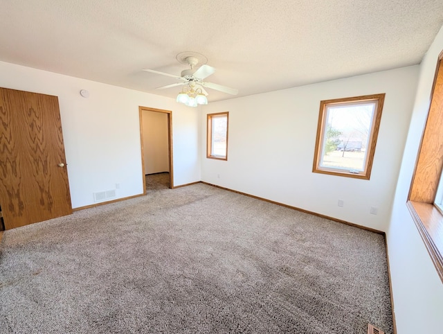 unfurnished room featuring visible vents, a textured ceiling, carpet flooring, baseboards, and ceiling fan