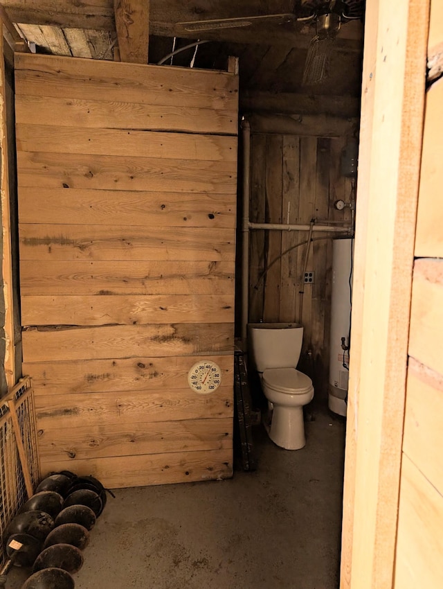 bathroom with wooden walls, gas water heater, toilet, and unfinished concrete flooring