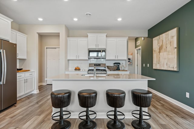 kitchen with backsplash, an island with sink, white cabinets, and appliances with stainless steel finishes