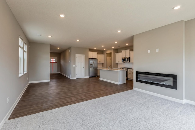 unfurnished living room with recessed lighting, dark carpet, and baseboards