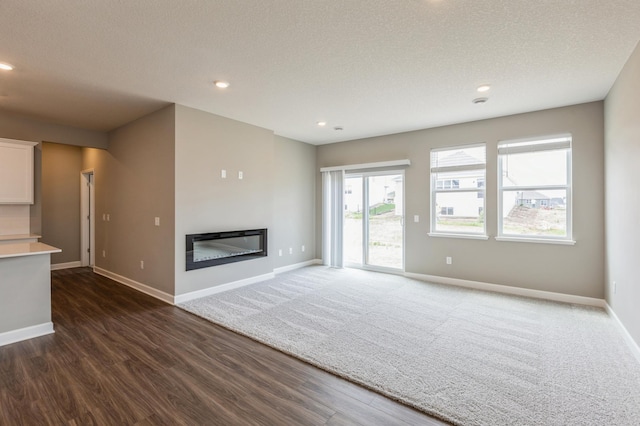 unfurnished living room with a glass covered fireplace, a textured ceiling, baseboards, and recessed lighting