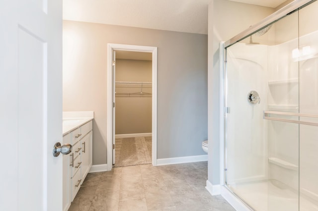 bathroom with baseboards, toilet, a spacious closet, vanity, and a shower stall