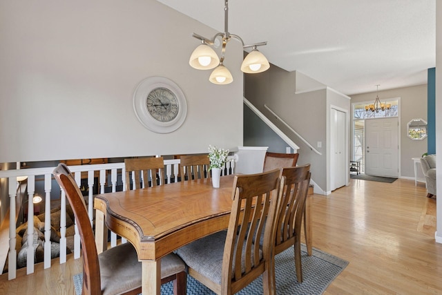 dining area featuring light wood-style flooring, baseboards, a chandelier, and stairs