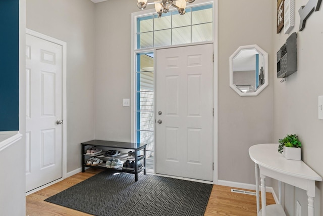 foyer featuring visible vents, baseboards, an AC wall unit, light wood-style floors, and a notable chandelier