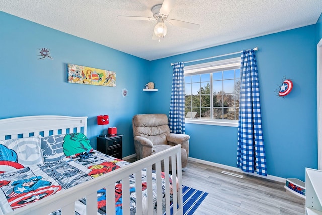 bedroom with a ceiling fan, visible vents, wood finished floors, baseboards, and a textured ceiling