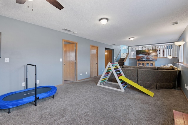 playroom with visible vents, a textured ceiling, carpet flooring, and a ceiling fan