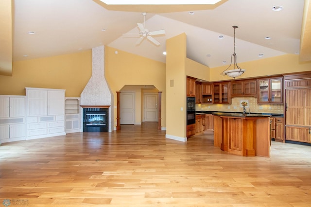 kitchen featuring a fireplace, decorative light fixtures, black double oven, ceiling fan, and light hardwood / wood-style flooring