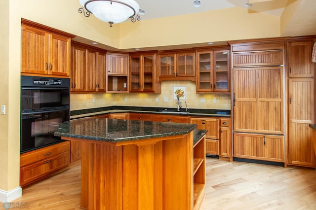 kitchen featuring sink, a center island, black double oven, dark stone counters, and light hardwood / wood-style floors