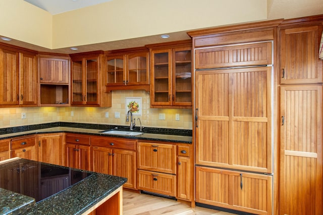 kitchen with tasteful backsplash, sink, dark stone countertops, and light wood-type flooring