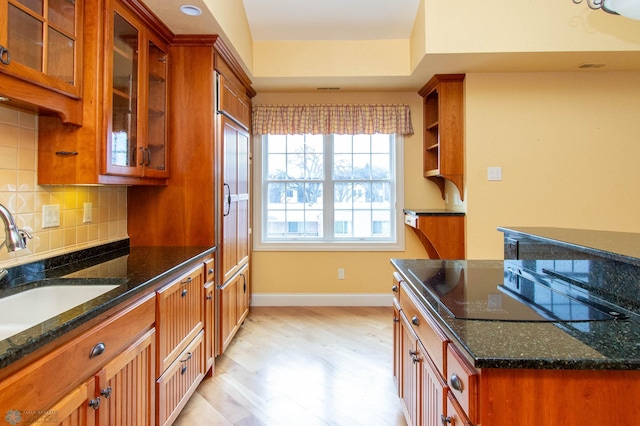 kitchen with sink, dark stone countertops, black electric stovetop, light hardwood / wood-style floors, and backsplash