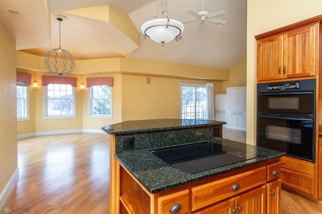 kitchen featuring pendant lighting, a center island, black appliances, dark stone counters, and light wood-type flooring