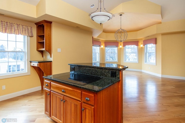 kitchen featuring decorative light fixtures, dark stone countertops, a center island, black electric stovetop, and light hardwood / wood-style flooring