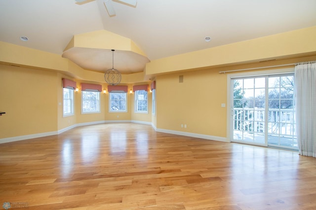 spare room featuring lofted ceiling, ceiling fan with notable chandelier, and light wood-type flooring