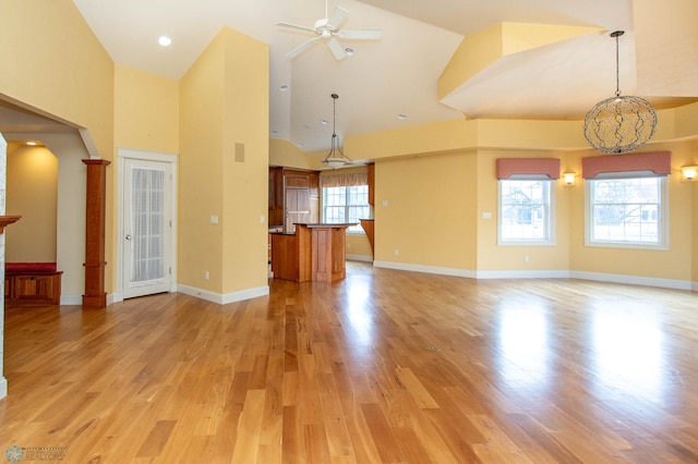 unfurnished living room featuring high vaulted ceiling, ceiling fan with notable chandelier, and light hardwood / wood-style floors