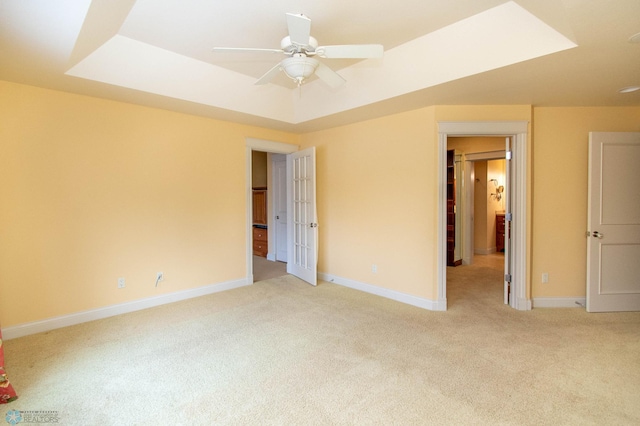 spare room featuring a raised ceiling, light colored carpet, and ceiling fan