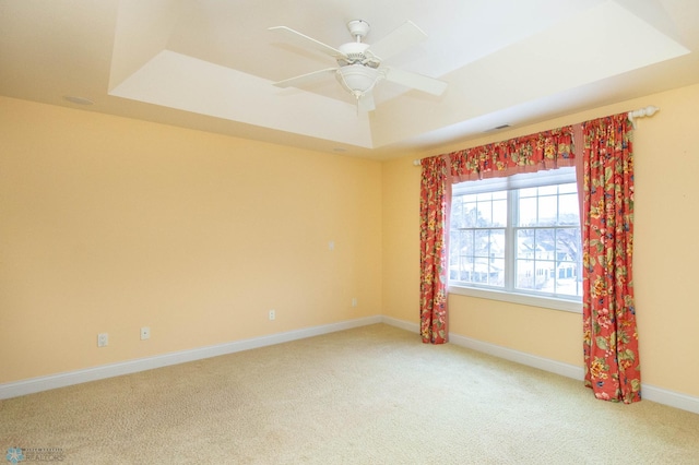 carpeted spare room with ceiling fan and a tray ceiling