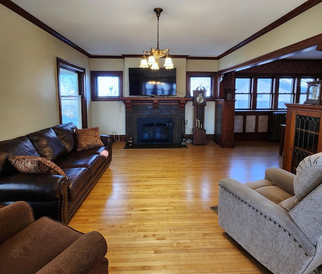 living room with a fireplace with flush hearth, ornamental molding, wood finished floors, and an inviting chandelier