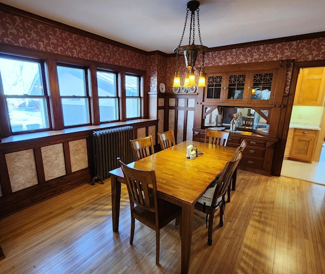 dining area with crown molding, light wood finished floors, radiator heating unit, a chandelier, and wallpapered walls