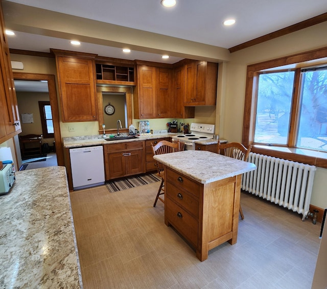 kitchen featuring radiator, brown cabinetry, a sink, white appliances, and a kitchen breakfast bar