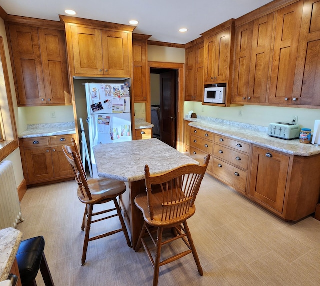 kitchen with white appliances, brown cabinetry, radiator heating unit, a kitchen breakfast bar, and a center island