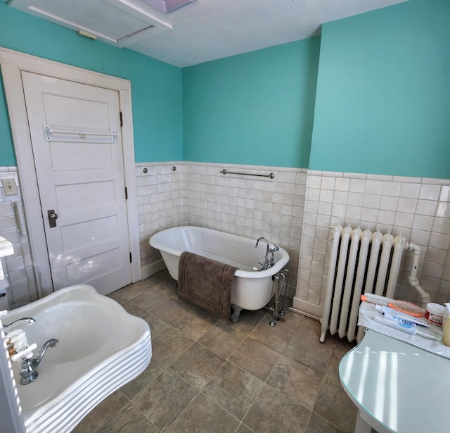 bathroom featuring radiator, wainscoting, a soaking tub, and tile walls