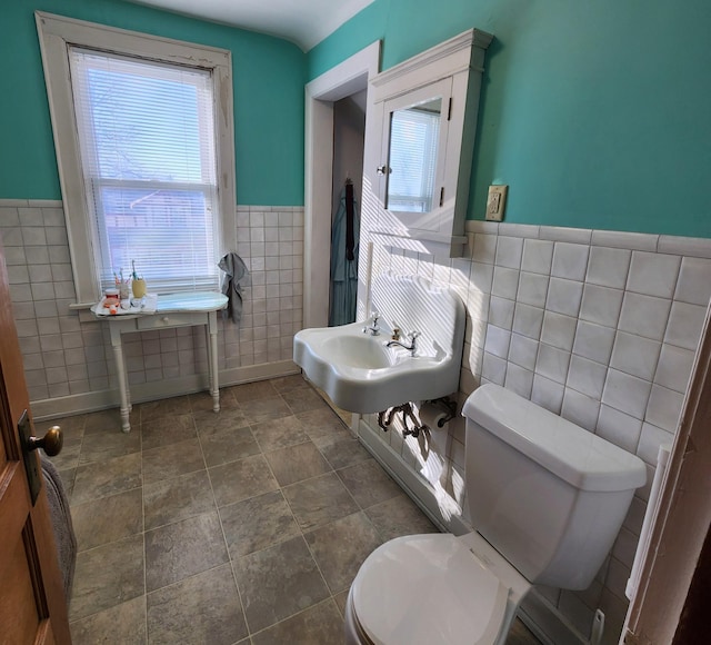 bathroom featuring toilet, tile walls, a sink, and wainscoting