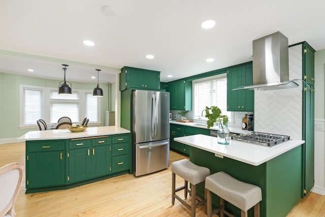 kitchen featuring a center island, green cabinets, light hardwood / wood-style floors, stainless steel appliances, and wall chimney range hood