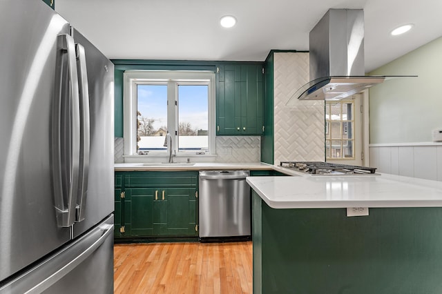 kitchen featuring sink, light stone counters, green cabinetry, island range hood, and stainless steel appliances