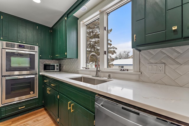 kitchen with sink, light stone counters, appliances with stainless steel finishes, green cabinets, and backsplash