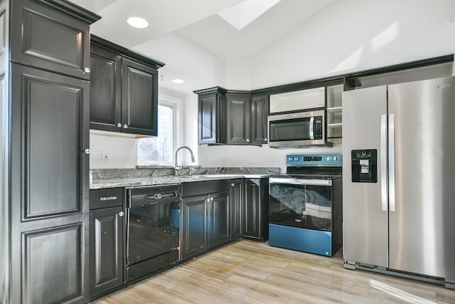 kitchen featuring light stone counters, stainless steel appliances, vaulted ceiling with skylight, and light hardwood / wood-style floors