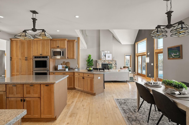 kitchen with a fireplace, a center island, stainless steel appliances, light hardwood / wood-style flooring, and pendant lighting