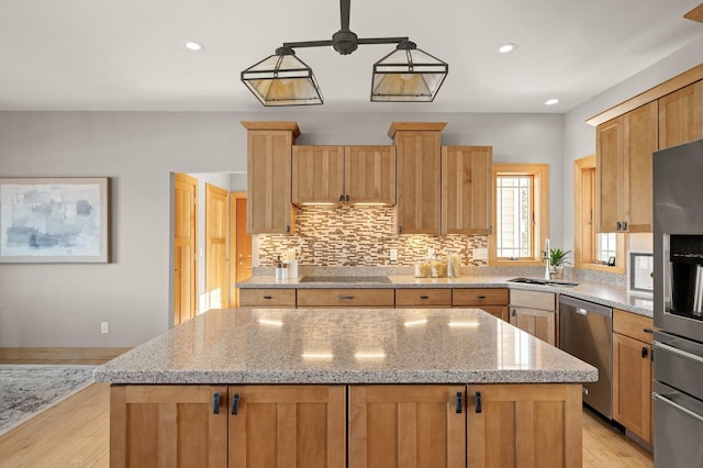 kitchen featuring appliances with stainless steel finishes, a kitchen island, sink, and light stone countertops