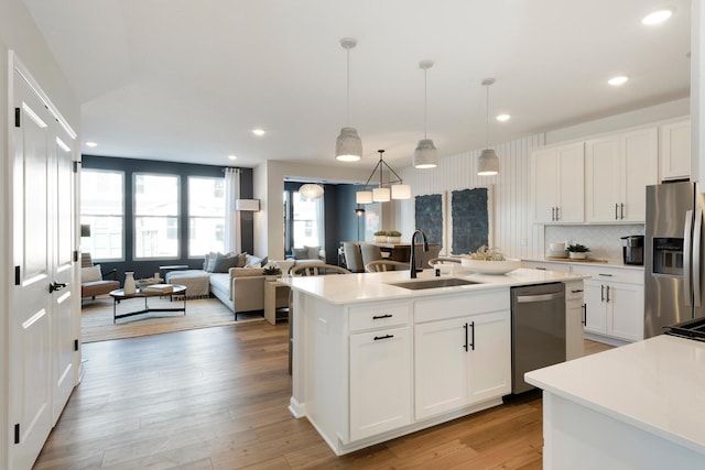 kitchen featuring sink, appliances with stainless steel finishes, white cabinetry, hanging light fixtures, and an island with sink