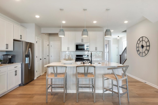 kitchen featuring a center island with sink, white cabinets, pendant lighting, stainless steel appliances, and backsplash