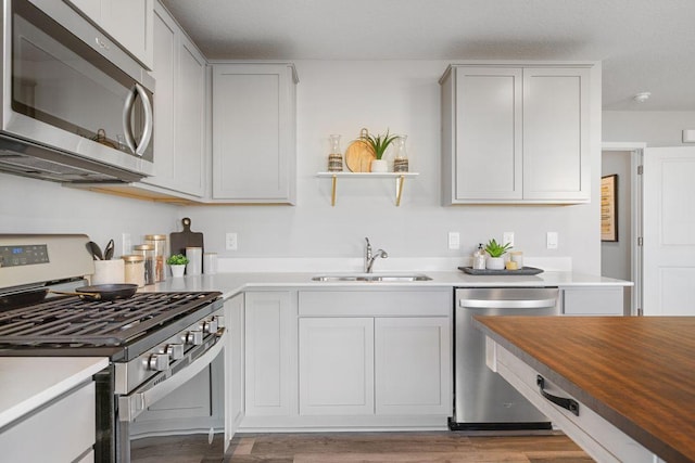 kitchen featuring open shelves, a sink, butcher block counters, stainless steel appliances, and light wood finished floors