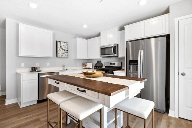 kitchen with white cabinets, a sink, stainless steel appliances, and light wood-style flooring