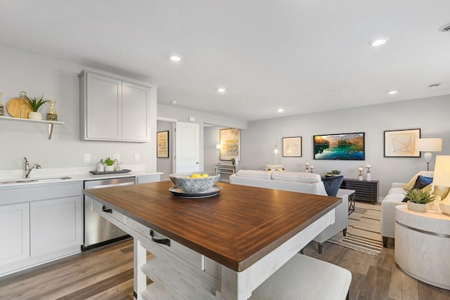 kitchen with recessed lighting, light wood finished floors, open shelves, stainless steel dishwasher, and a sink