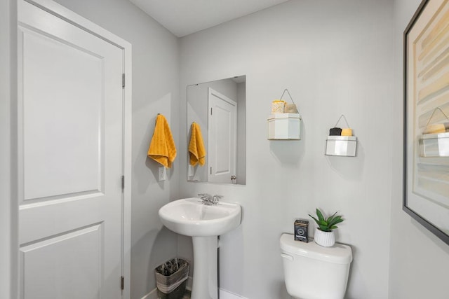 half bathroom with baseboards, a sink, and toilet