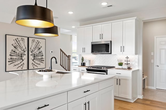 kitchen with sink, white cabinetry, light stone counters, appliances with stainless steel finishes, and pendant lighting