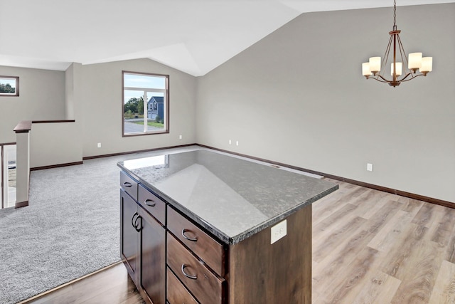 kitchen featuring hanging light fixtures, a center island, dark brown cabinetry, vaulted ceiling, and dark stone counters