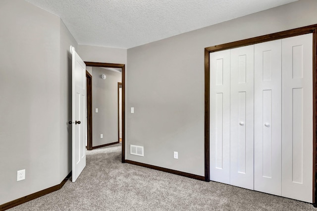 unfurnished bedroom with light colored carpet, a textured ceiling, and a closet