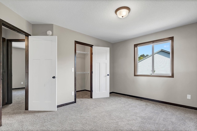 unfurnished bedroom with a spacious closet, light colored carpet, a textured ceiling, and a closet