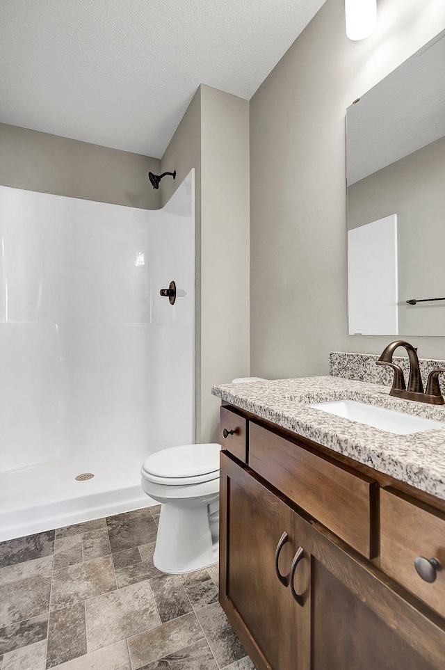 bathroom featuring vanity, a textured ceiling, toilet, and walk in shower